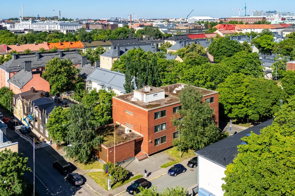 Kolmikerroksinen tiilinpunainen toimitilakiinteistö Helsingin Vallilan puutaloalueella.