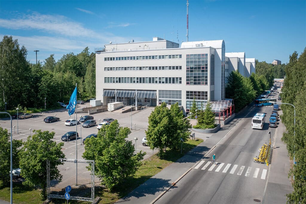 Vaaleajulkisivuinen toimitilakiinteistö Laippatie 4 Helsinki kuvattuna idän kulmakta. Talon pihalla on pysäköintialue ja kadulla kaupunkipyöräasema.