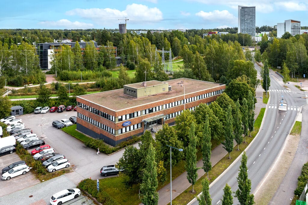 Espoon Olarinluoma 7 ilmakuvassa. Punatiilinen toimitilakiinteistö, jolla reilusti pysäköintitilaa.