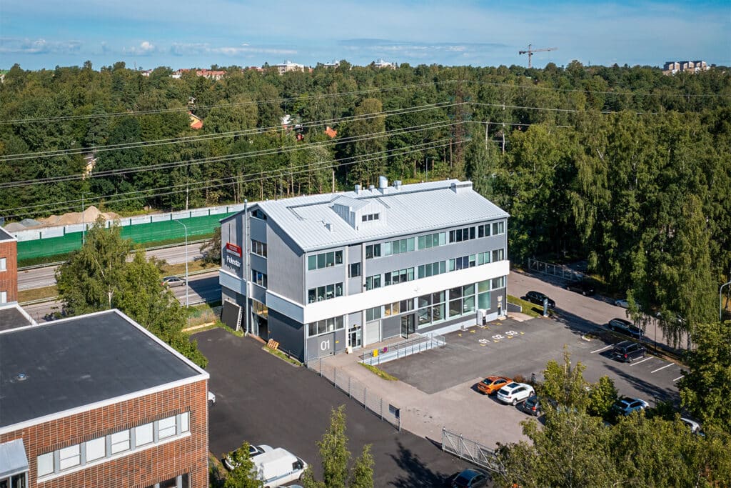 Viistosti ilmasta kuvattu toimitilakiinteistö Helsingin Lämmittäjänkatu 6. Rakennuksen edustalla on asfaltoitu pysäköintialue.